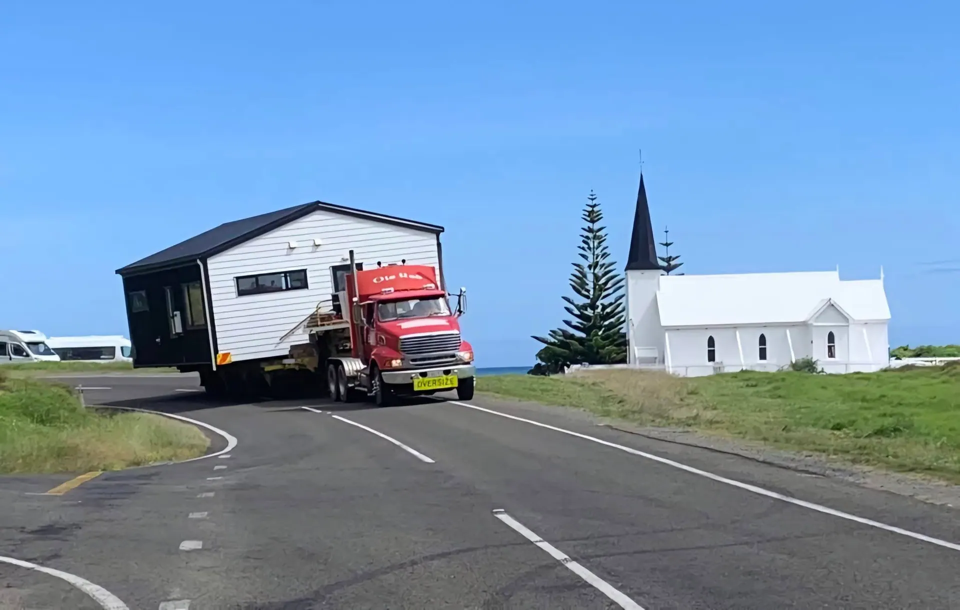 House transport on coastal road passing landmark church in New Zealand